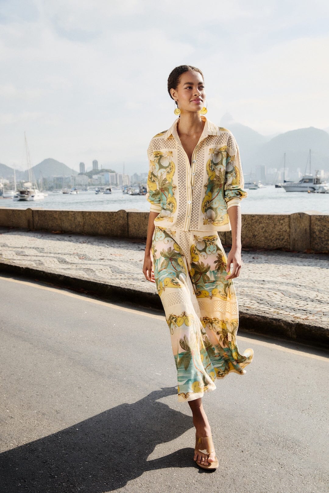 Model in a printed Farm Rio linen shirt and wide-leg trousers walking along the Rio waterfront