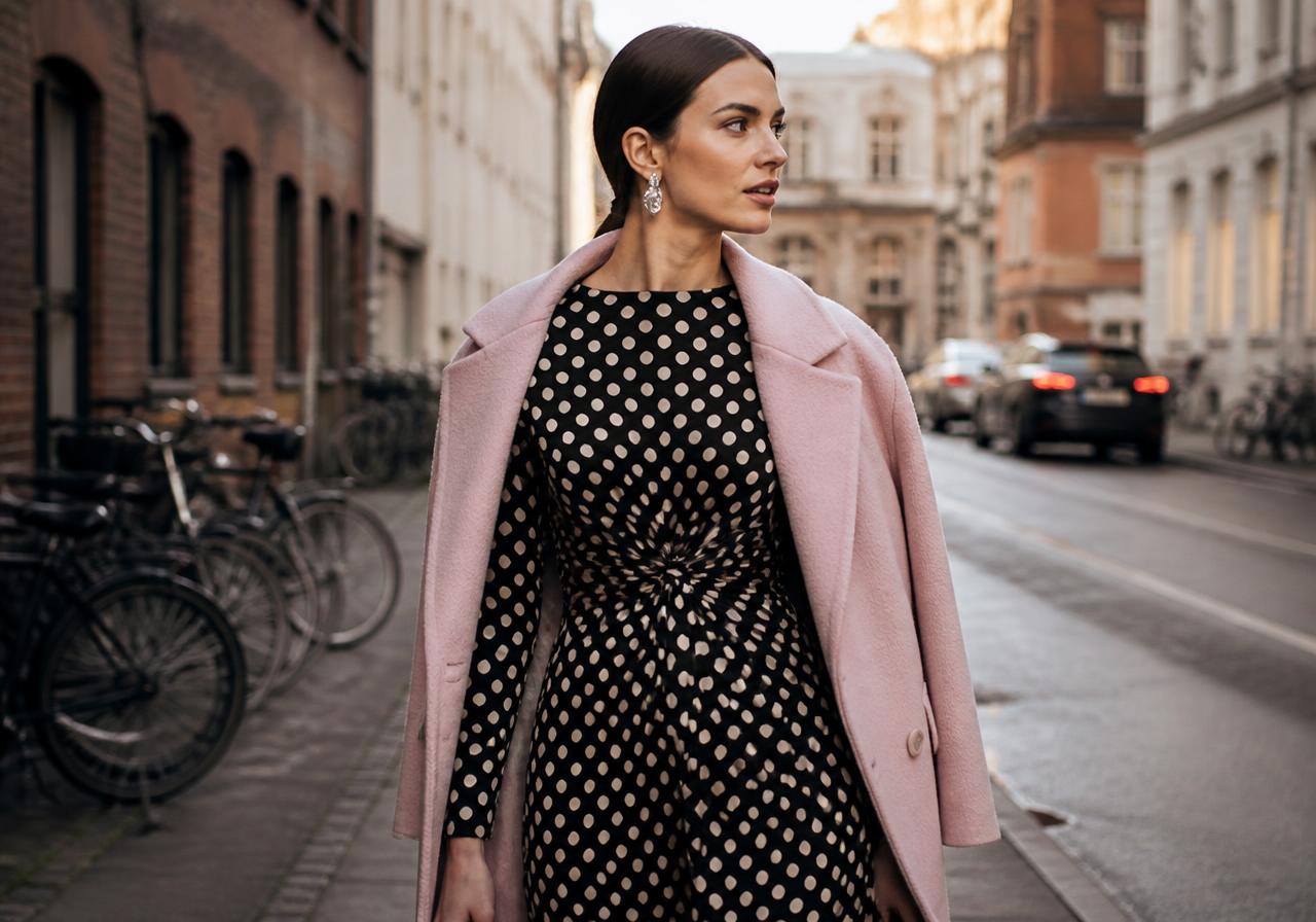 Scandinavian fashion trends SS27: black and cream polka dot dress worn with a pastel pink coat and sculptural earrings in Copenhagen
