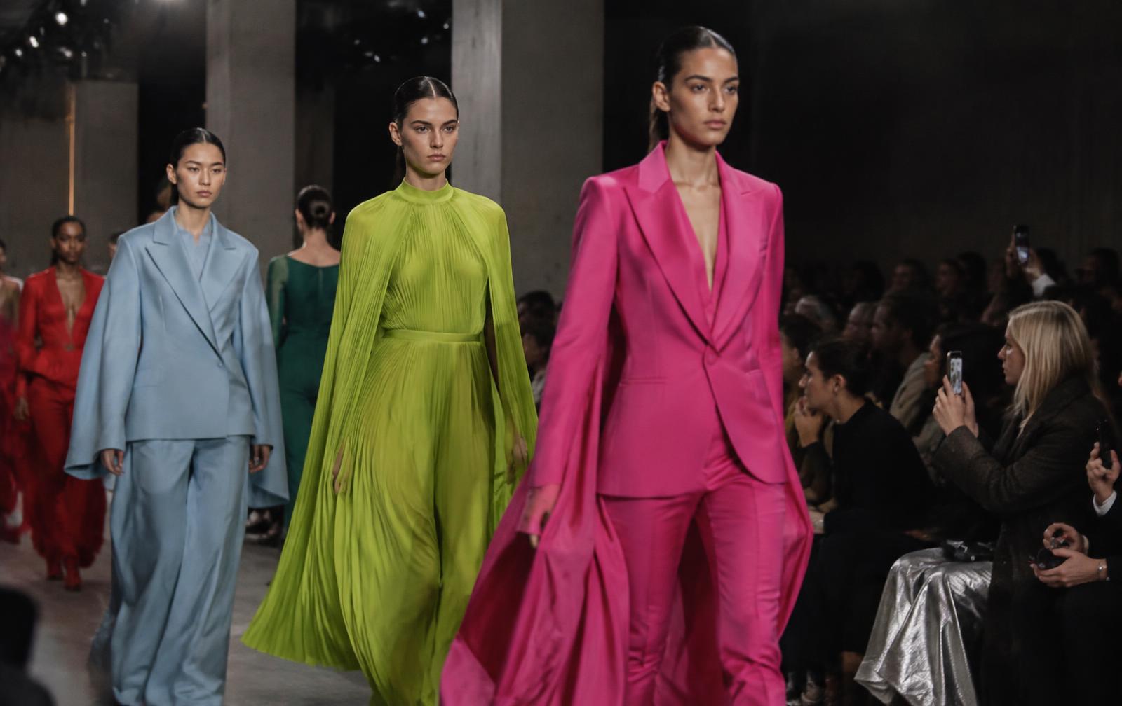 Three models on a runway in powder-blue tailoring, an acid-green dress and a hot-pink suit