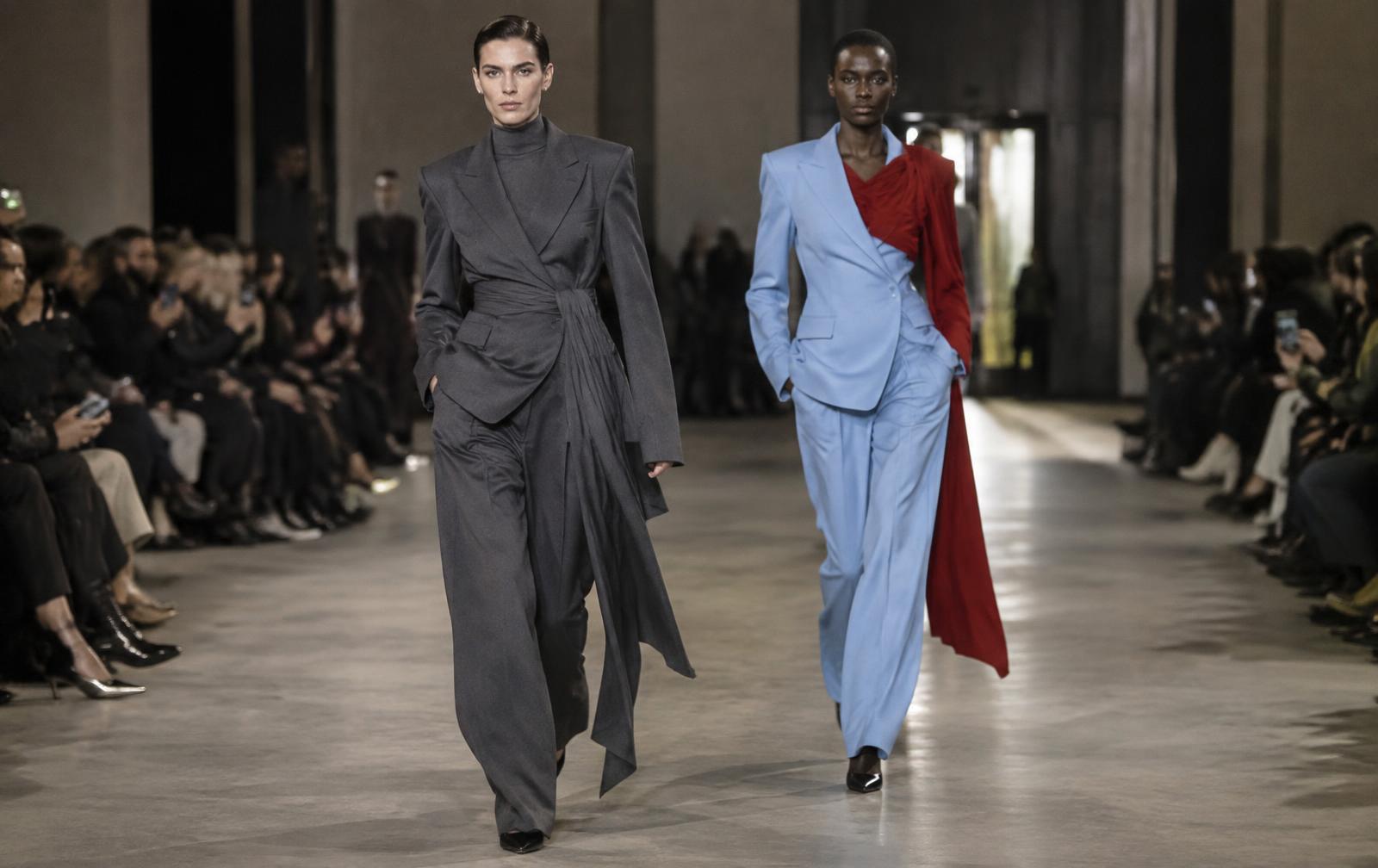 Two runway-style silhouettes contrasting a charcoal structured jacket with a pale blue tailored suit and red layer