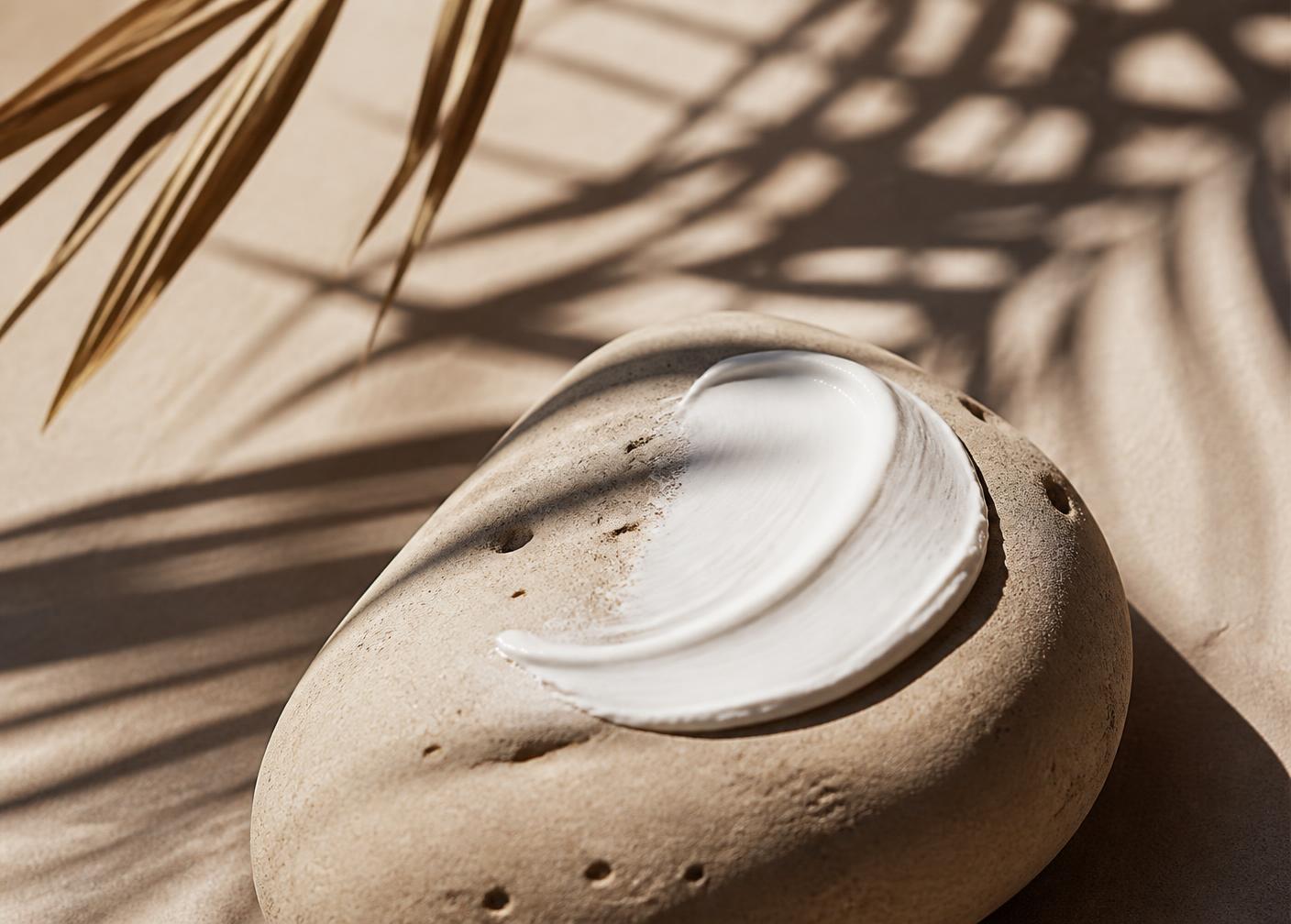 A smear of white sunscreen cream on a smooth sand-colored stone in bright sunlight