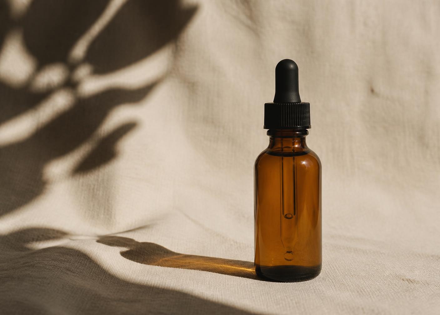 An amber glass serum dropper bottle casting a sculptural shadow on cream linen