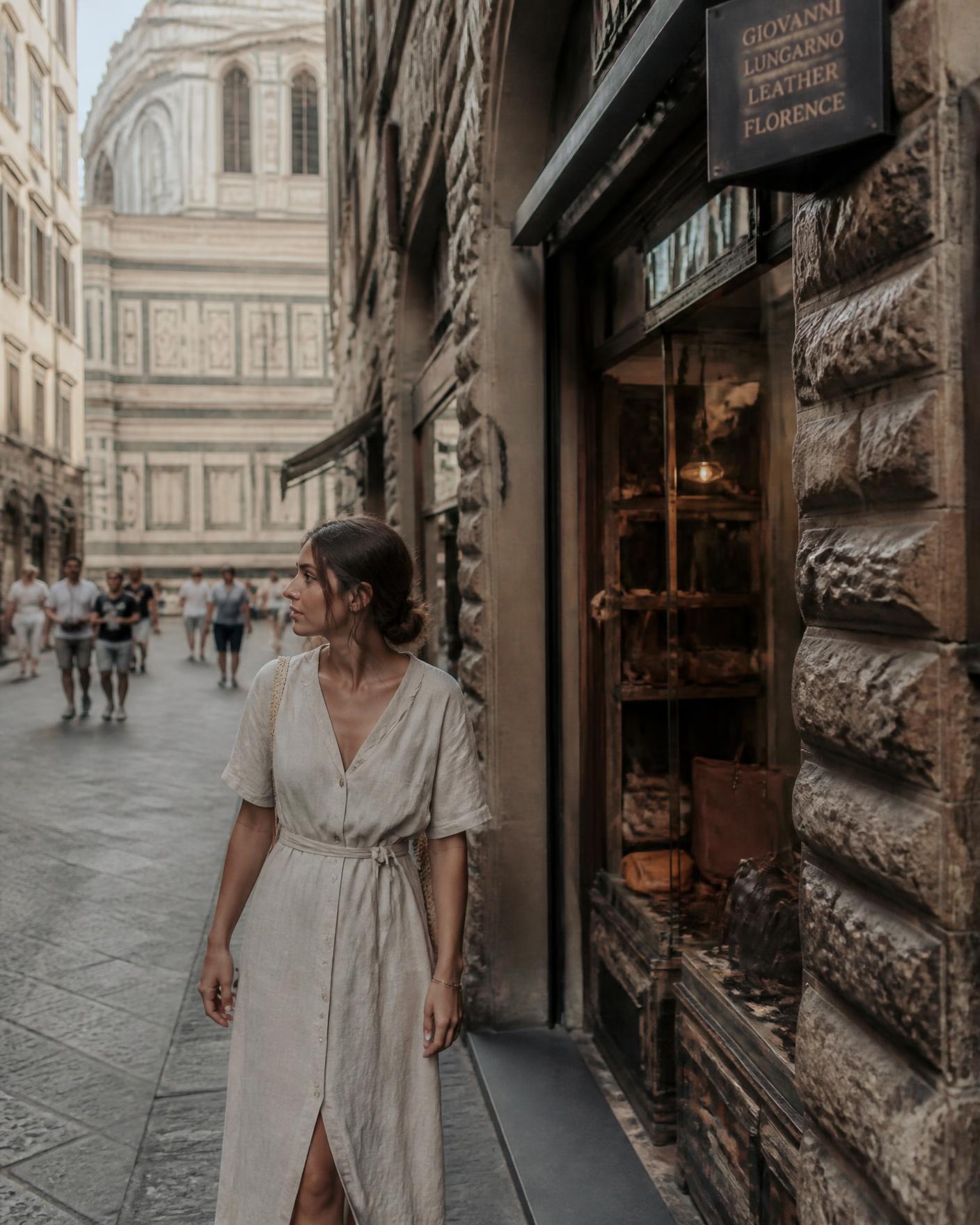 A woman in a linen dress walking past an artisan leather shop in a Florence street with the Duomo behind