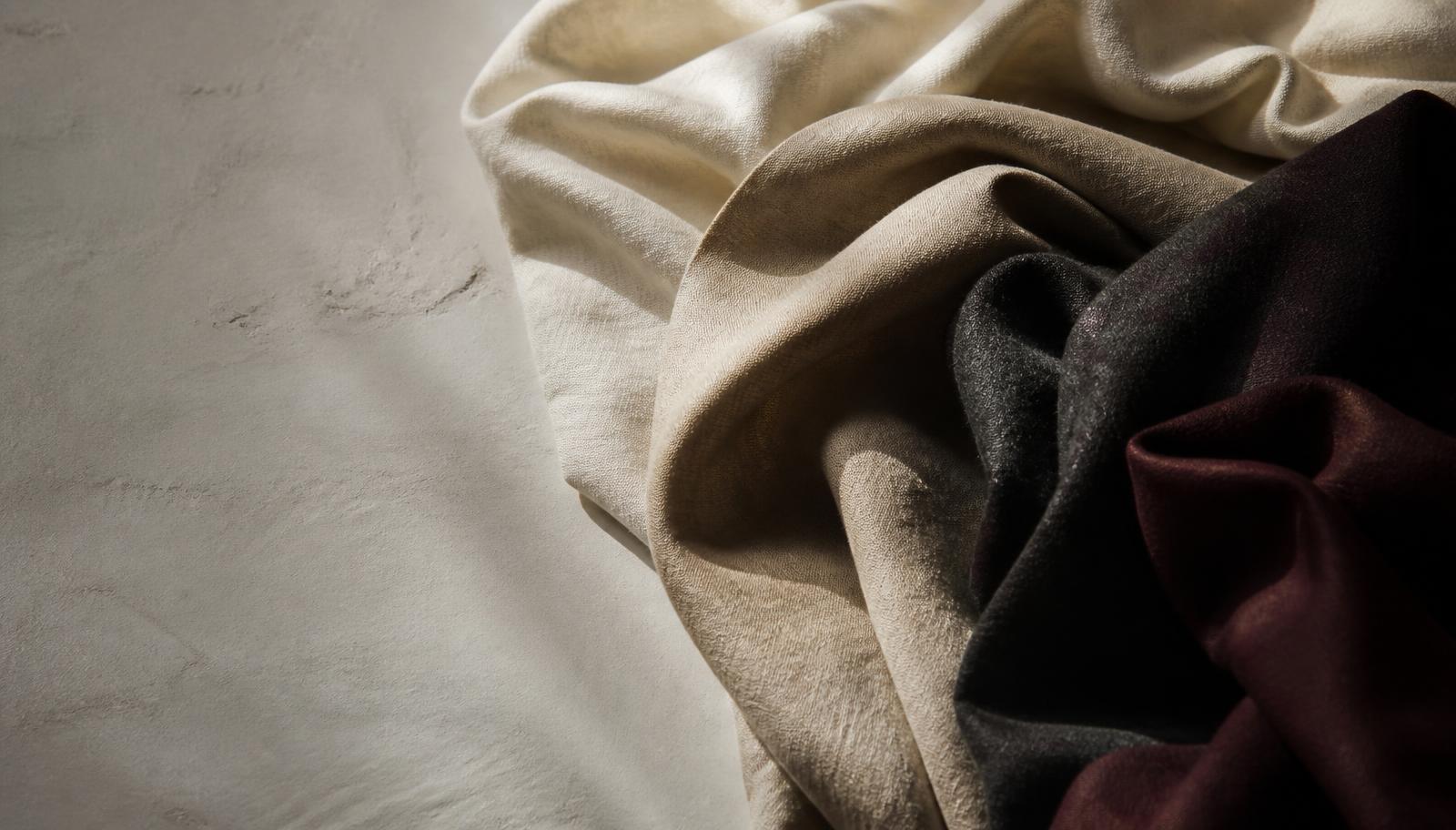 Draped ivory, sand, charcoal and burgundy fabric swatches photographed as a trend forecasting still life